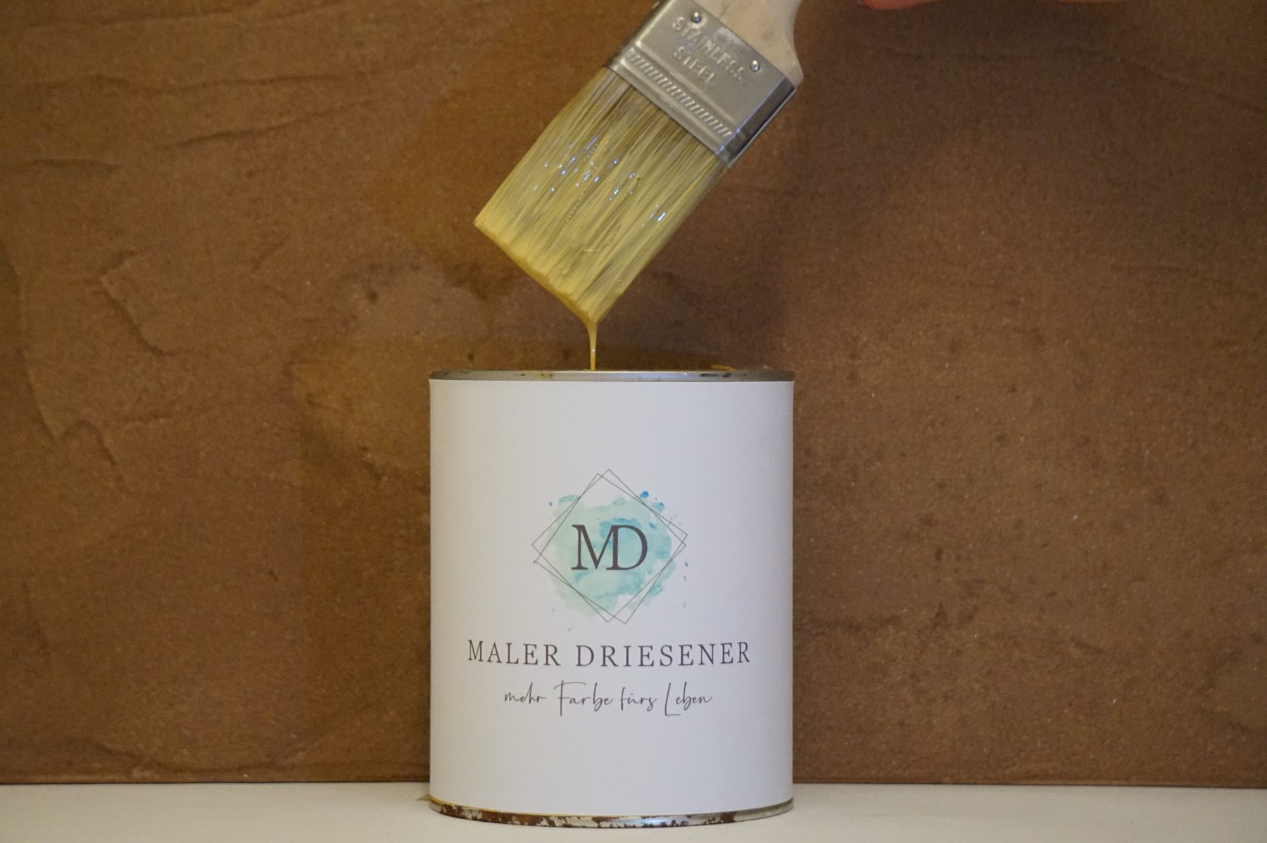 Farbdose mit dem Maler-Driesener-Logo und ein Pinsel mit gelber Farbe