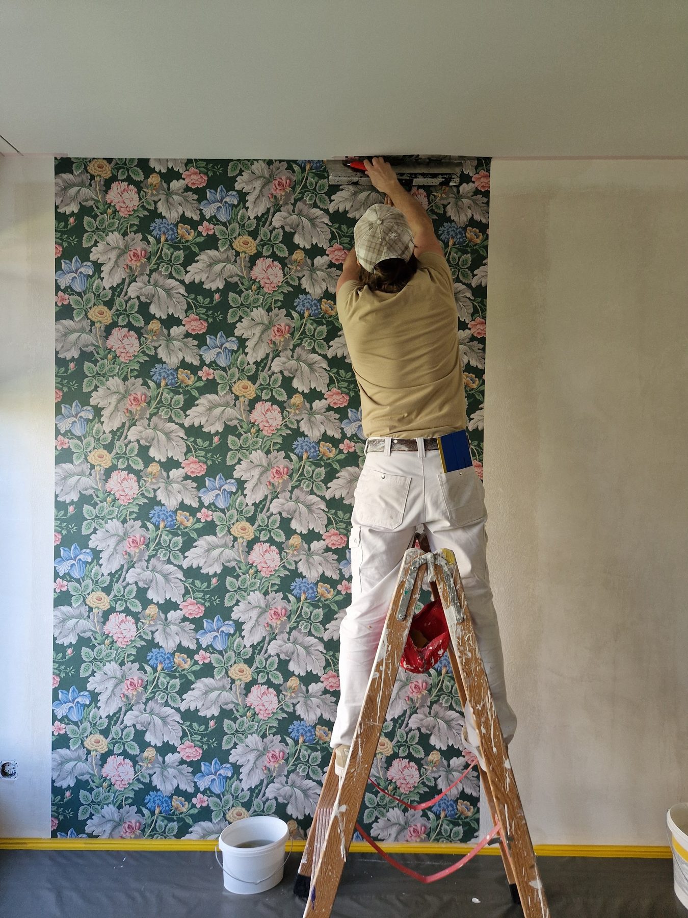Maler tapeziert eine Blumentapete auf der Leiter